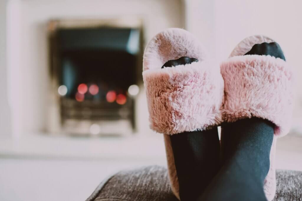 Black stocking feet in pink slippers in front of fireplace for introverted home design.